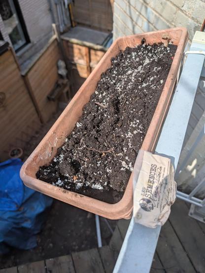 A trough with soil and seeds, on a balcony railing
