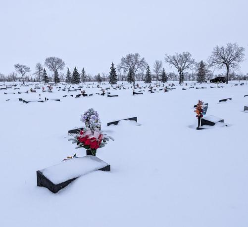 A prairie cemetery The markers are mostly snow-covered; the two nearest have bouquets, dusted with snow.