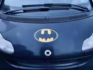 The Batmobile insignia on the hood of a dark blue Smart car.