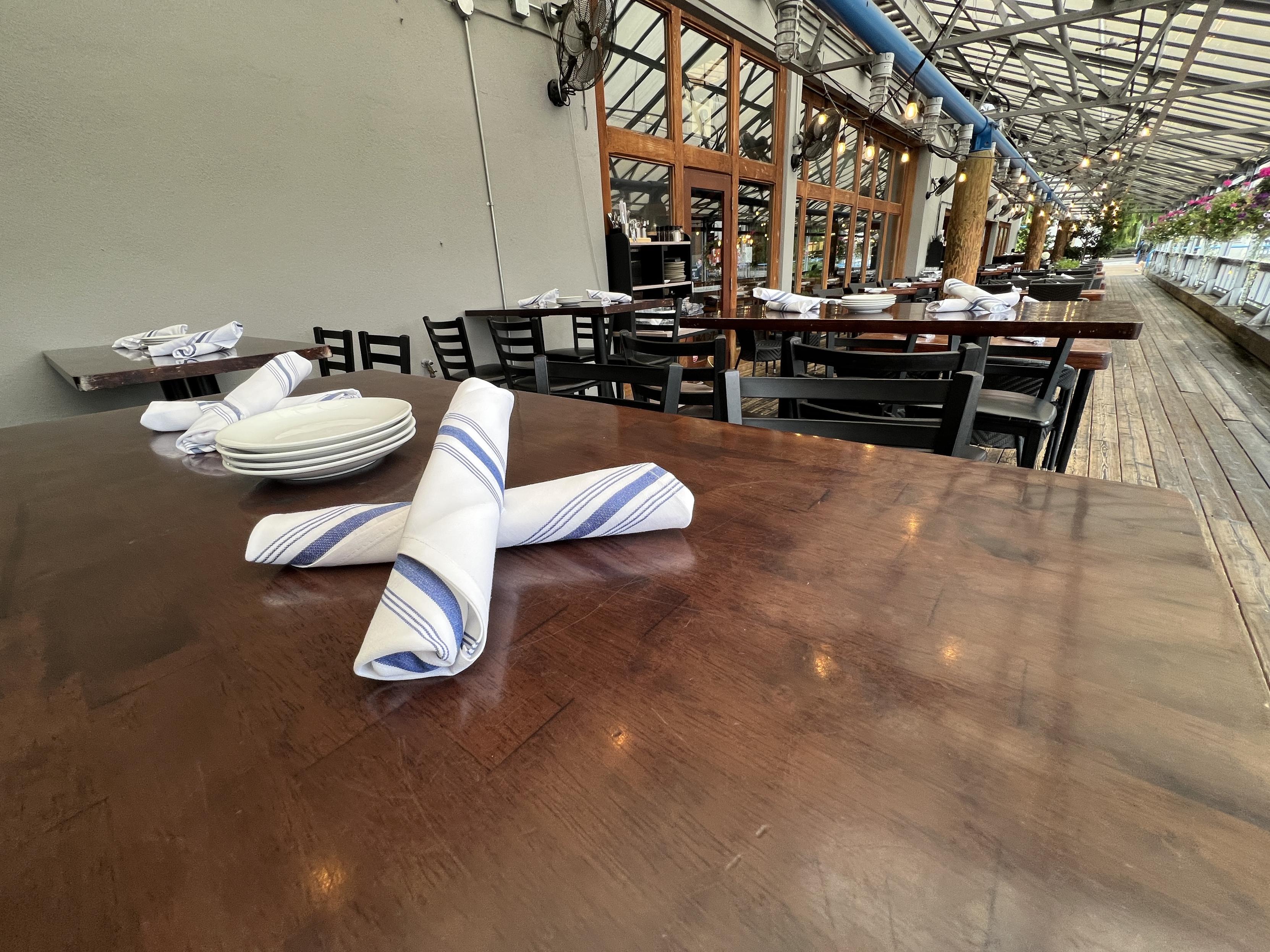 Cutlery wrapped in white napkins sit on a wooden table of a restaurant’s outdoor seating area.