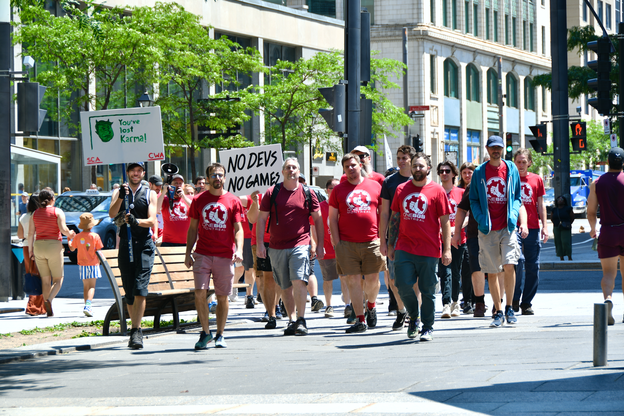 Des membres de OneBSG avec pancartes et chandails rouges marchent le long de la rue pour rejoindre d'autres allié'e's à la Place Square Victoria au centre-ville de Montréal.